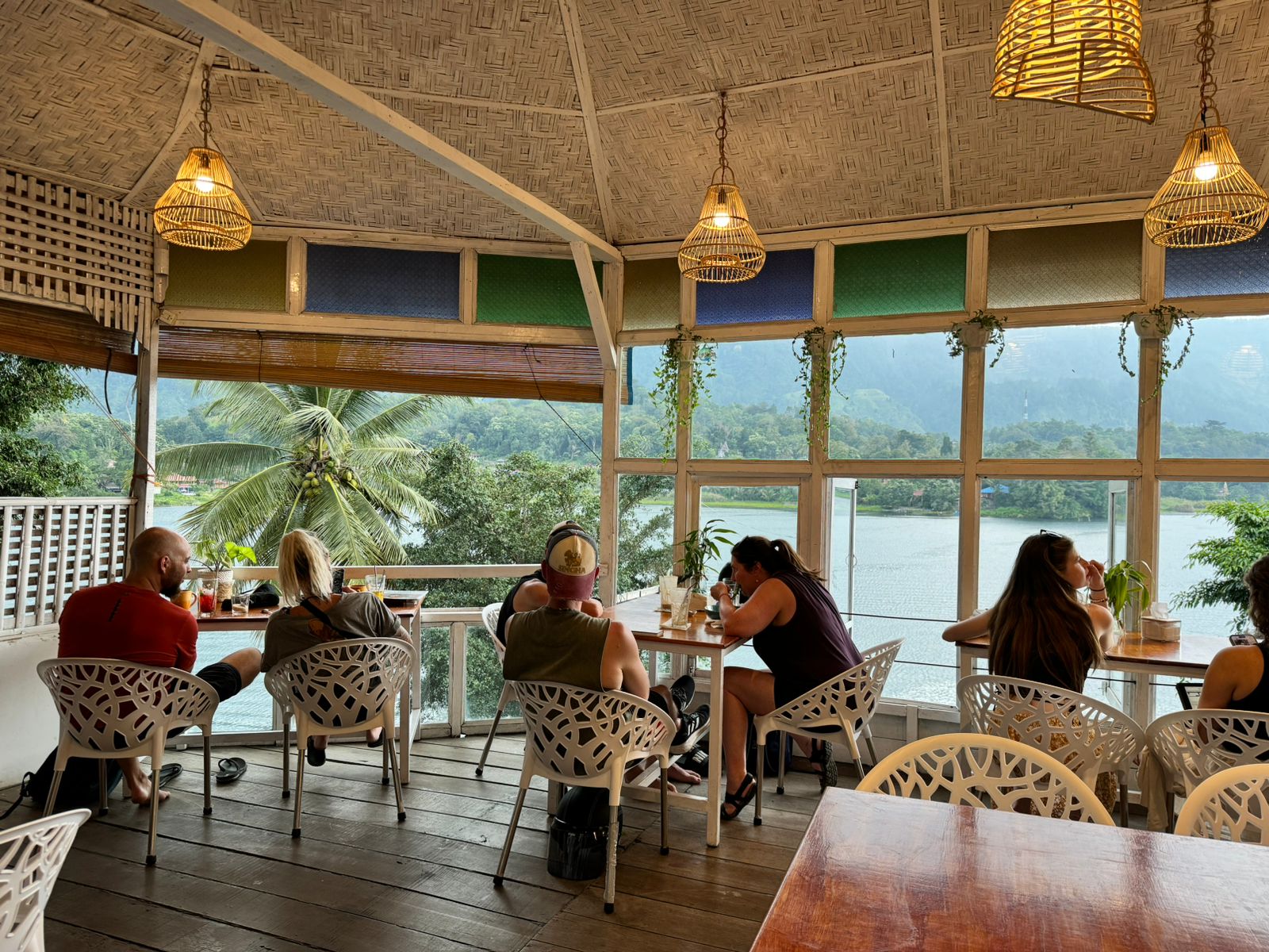 Guests at the café tables with rattan lamps and Lake Toba views
