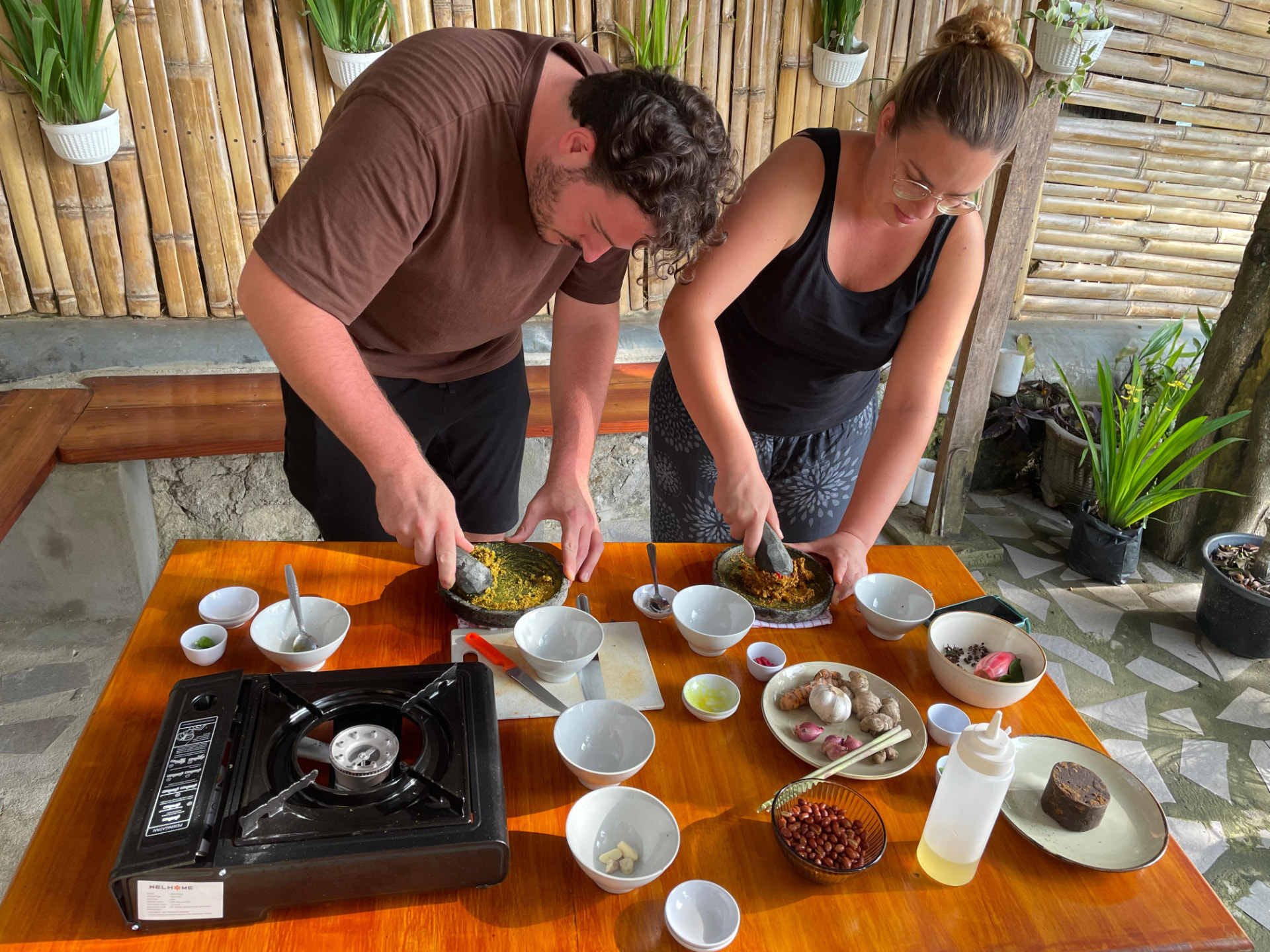 Two guests grinding sambal in stone mortars side by side